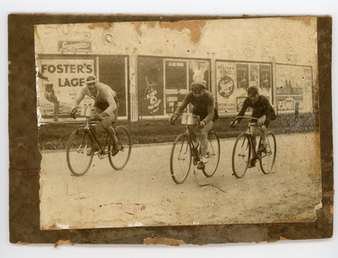 Photograph - Black and White Photograph, Three Cyclists riding past Billboards, 1930s