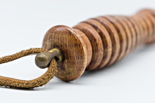 A brass eyelet attached to the end of a golden coloured wooden truncheon with a leather cord threaded through it