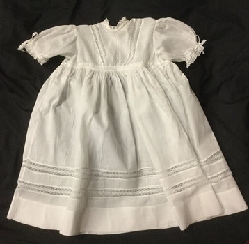 White child's dress with short puffed sleeves, high waistline, and lace inserts, on black background.