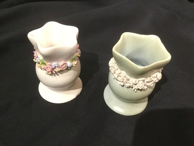 Two small, glazed pottery vases. One green with cream flowers, and one white with multi-coloured flowers.