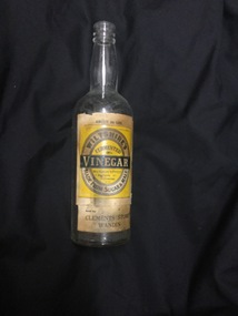 A tall clear glass Wiltshire's vinegar bottle with a cream, yellow and black paper label. 