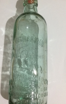 A large green tinted Marchant's soft drink bottle with a pink plastic screw in stopper.