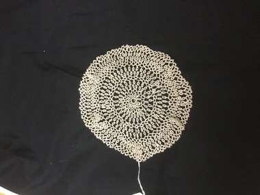 White lacy doily on black background.
