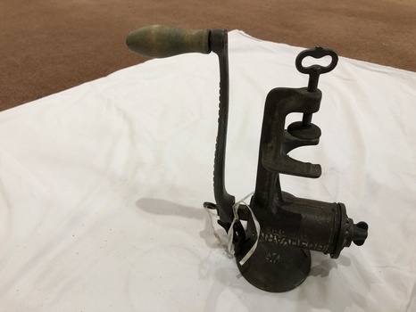 A vintage cast iron mincer with a brown wooden handle attached to the long cast iron handle.