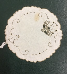 A round cream linen doily with khaki coloured floral embroidery, open cut pattern and a scalloped edge.