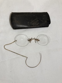 A pair of rimless spectacles with a metal chain and shaped earpiece.  It has a black snap case.