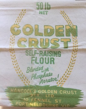 A vintage white calico flour bag with the brand Golden Crust Self-Raising Flour printed in yellow and green lettering on the front.