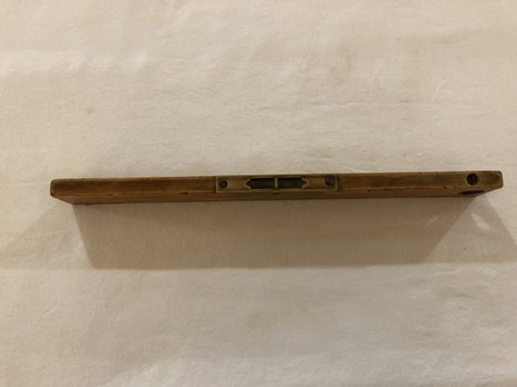 A vintage wooden spirit level used in carpentry with two spirit levels set in brass; one in the middle on the side and one at the end. 