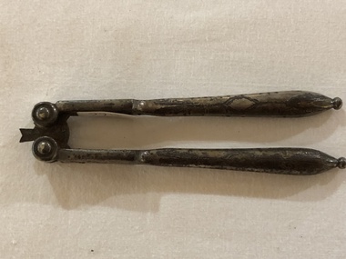 Metal folding hinged nutcracker with decorative engraving on the handles.