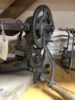 Cast iron grain sickle with hand-cranked wooden handle, stone grinder head, and 4 wheels, on a wooden base.