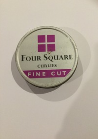 A round, silver coloured Four Square Curlies brand tobacco tin with a removable lid.
