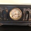 A black wooden cased mantel clock with Roman classical design on the front and sides. 