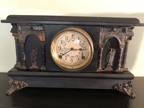 A black wooden cased mantel clock with Roman classical design on the front and sides. 