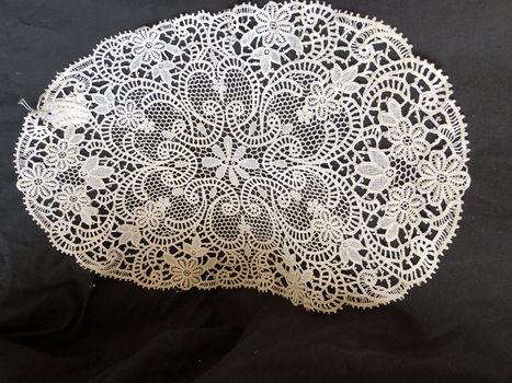 A highly decorated crocheted floral and swirl patterned oval doily.