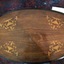 An antique brown oval table with inset gold coloured wooden ornate urns and a double lined pattern around the edge on the top.