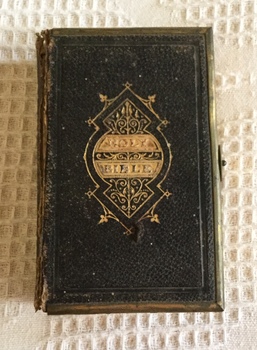 A small holy bible with a decorative front cover and metal clasp.