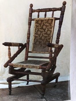 An elaborate turned wooden framed rocking chair with spring 'rockers' and fabric on the seat, back and on arms.