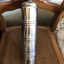 A stainless steel, cylindrical bed warmer, with a removable screw stopper which has a looped handle on top. 