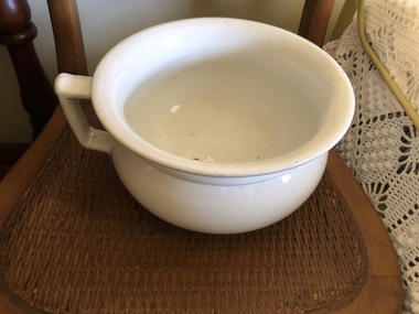A white ceramic chamber pot with a handle on the side.