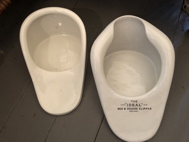 Two white vintage ceramic bed and douche slippers for use by invalids.