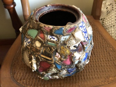 A handmade decorative pot with coloured ceramic pieces glued all over it.