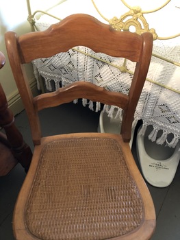 A brown wooden dining chair with a tan rattan woven seat.