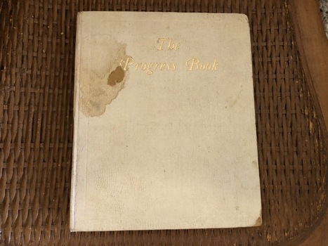 The cream covered book has the title The Progress Book in gold lettering on the front.