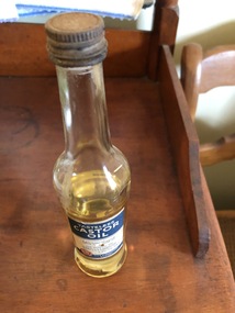 A tall clear glass bottle half filled with Castor Oil for medicinal purposes. It has a rusted metal screw top lid and a label for use.