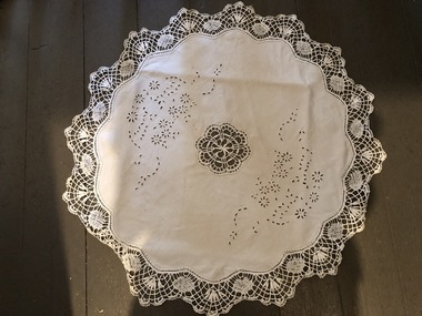 A round cotton tablecloth with crocheted edging and a pattern in the middle and dainty flowers.