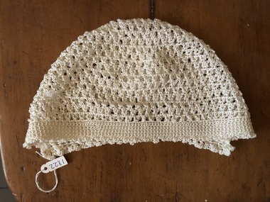 A cream silk hand crocheted baby bonnet with a 2.5cm patterned band at the edge.