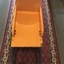 A yellow and blue painted wooden child's wheelbarrow with a wicker back and two pram wheels.