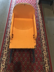 A yellow and blue painted wooden child's wheelbarrow with a wicker back and two pram wheels.