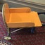A wooden homemade yellow and blue painted child's wheelbarrow with a metal frame and two pram wheels.