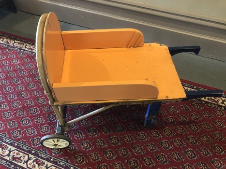 A wooden homemade yellow and blue painted child's wheelbarrow with a metal frame and two pram wheels.