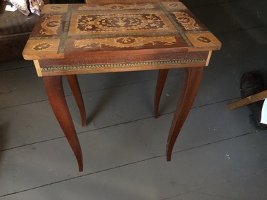 A highly decorative wooden music box table with colourful inlaid wood on the lid and sides and inside is a recessed wooden box.