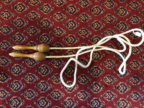 A white skipping rope with two wooden turned handles which are narrow at the end where you hold them.