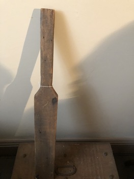 A child's handmade wooden cricket bat with a large crack in the handle.
