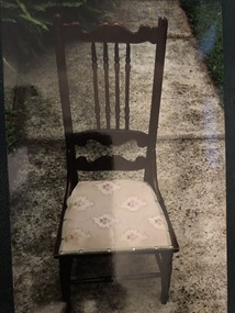 A brown wooden upholstered chair with decorative carved back supports and a coloured fabric cushion.