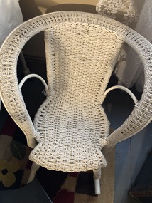 A white wicker child's rocking chair with arm rests and back all in one.