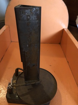 A rusty metal Designoscope or kaleidoscope with a long triangular tube connected to a flat stand at the bottom.