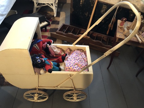 A vintage cream painted wooden and metal dolls pram with a hood, four wheels and a tubular long push curved handle. 