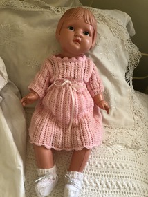 A celluloid baby doll wearing a pink knitted dress and withe knitted booties.