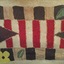 A small handmade highly patterned wool floor rug with red and brown stripes as well as green leaves and yellow flowers.