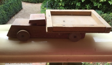 A brown painted handmade wooden toy truck with four wooden wheels, a cabin hood and a tray at the back.