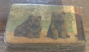 A green and brown painted chocolate tin with two dogs pictured on the lid.