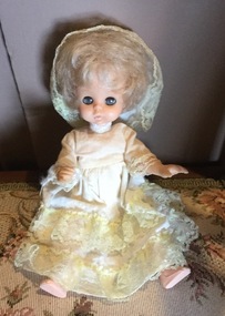 A small doll wearing a yellow dress and hat with lace borders.