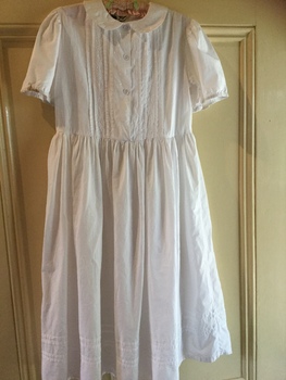 A white cotton girl's dress with embroidery, puffed sleeves, three buttons down the front and a flared skirt. 