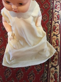 A cream woollen baby's dress with crotcheted edging around the sleeves and hem.