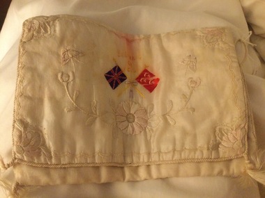 A cream satin embroidered handkerchief bag with a floral pattern and two flags on the front.