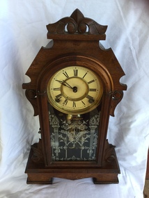 A dark brown highly carved mantel clock with a floral and column glass door.